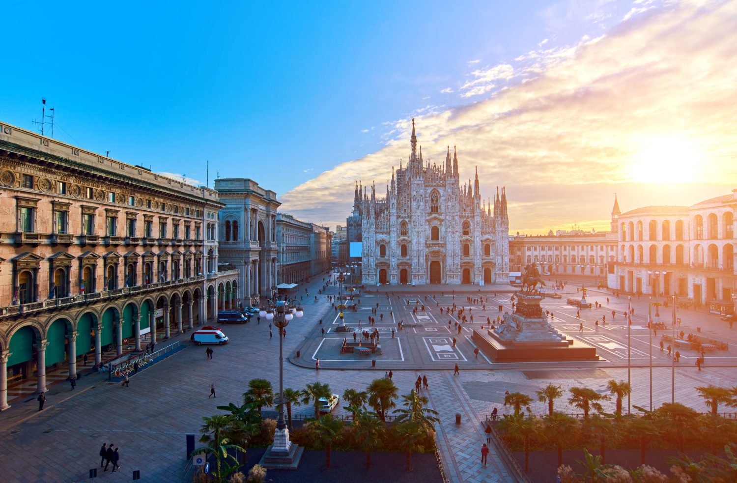 Sunset-lit European city square with arcaded buildings, palm trees, and a grand cathedral-style center building.
