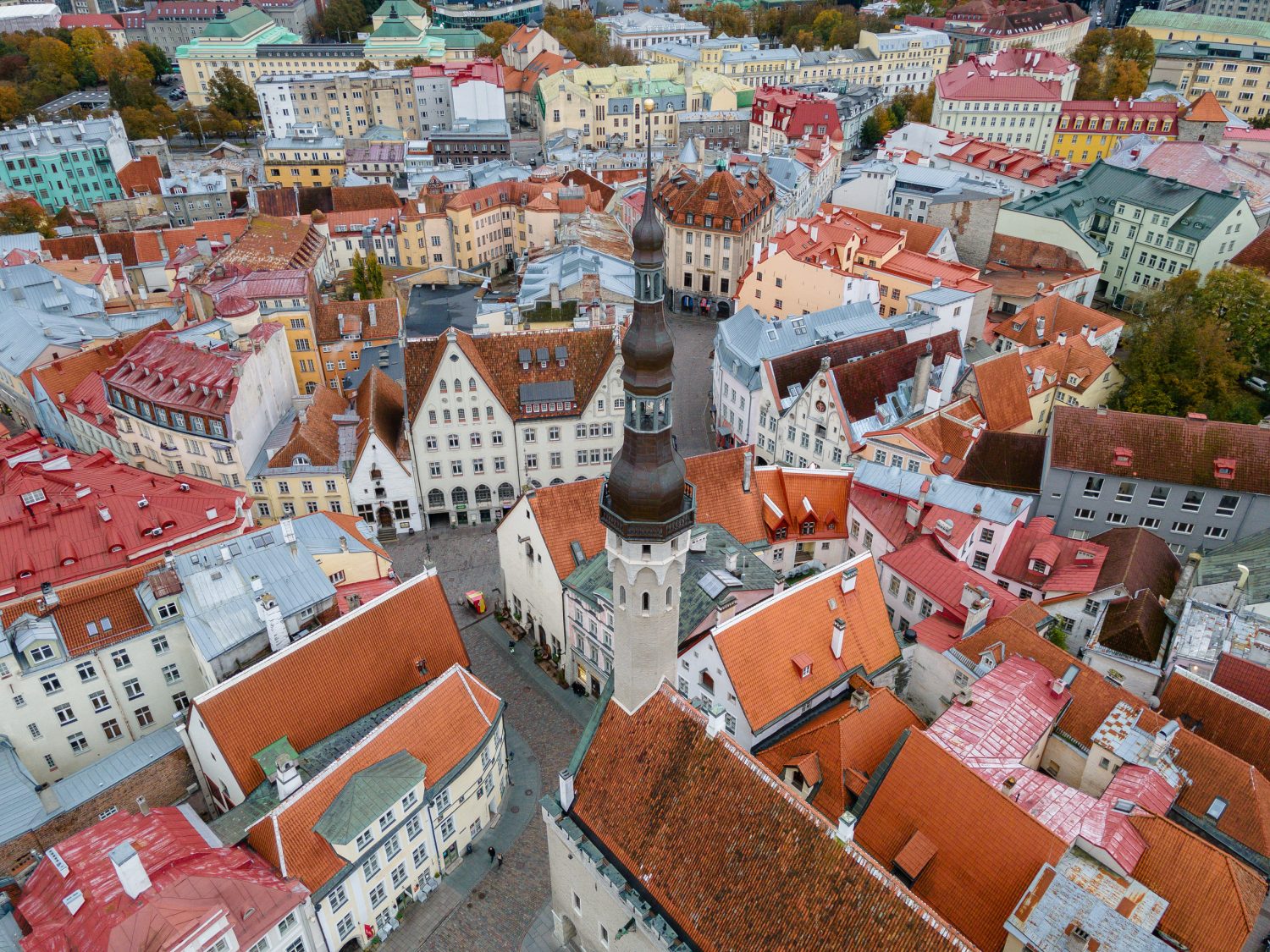 Aerial view of a colorful European town with pastel buildings and red-tiled roofs clustered around a tall church spire.