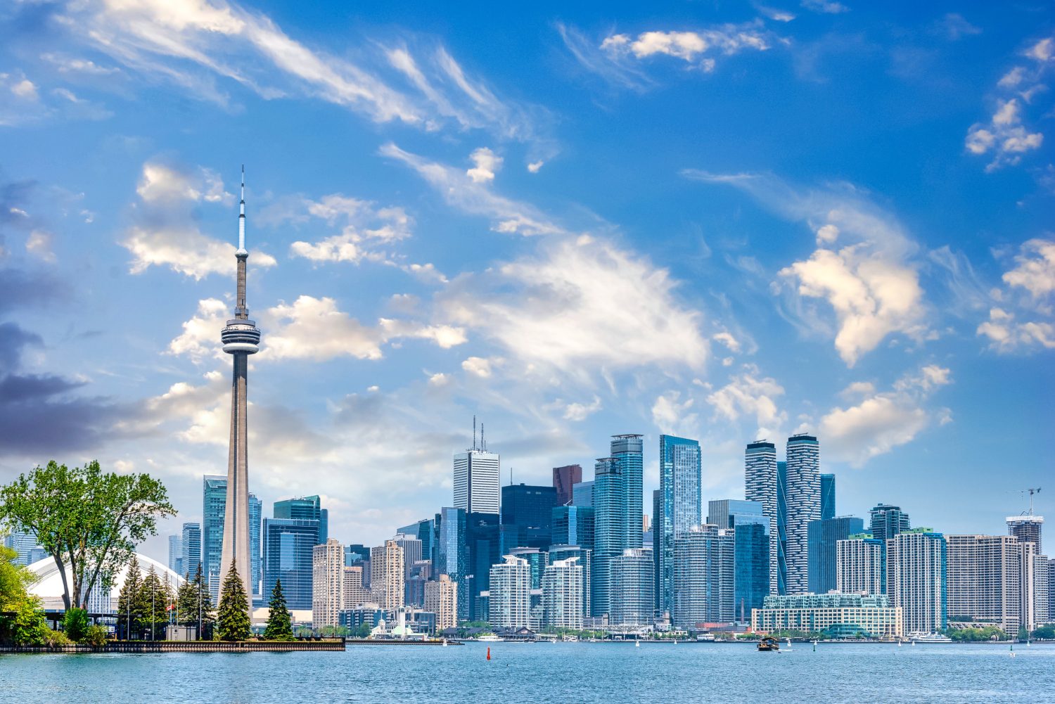 Toronto skyline with the CN Tower along a lakefront and modern high-rise buildings under a blue sky.