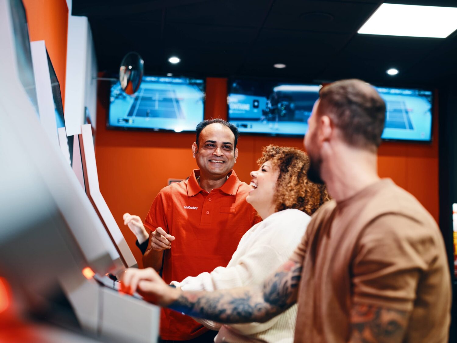 Three people stand around a large touchscreen arcade kiosk, smiling as they interact with the screen.