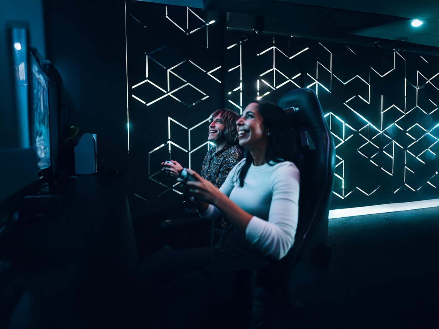 Two women in a dim, neon-lit room interact with a glowing geometric wall installation.