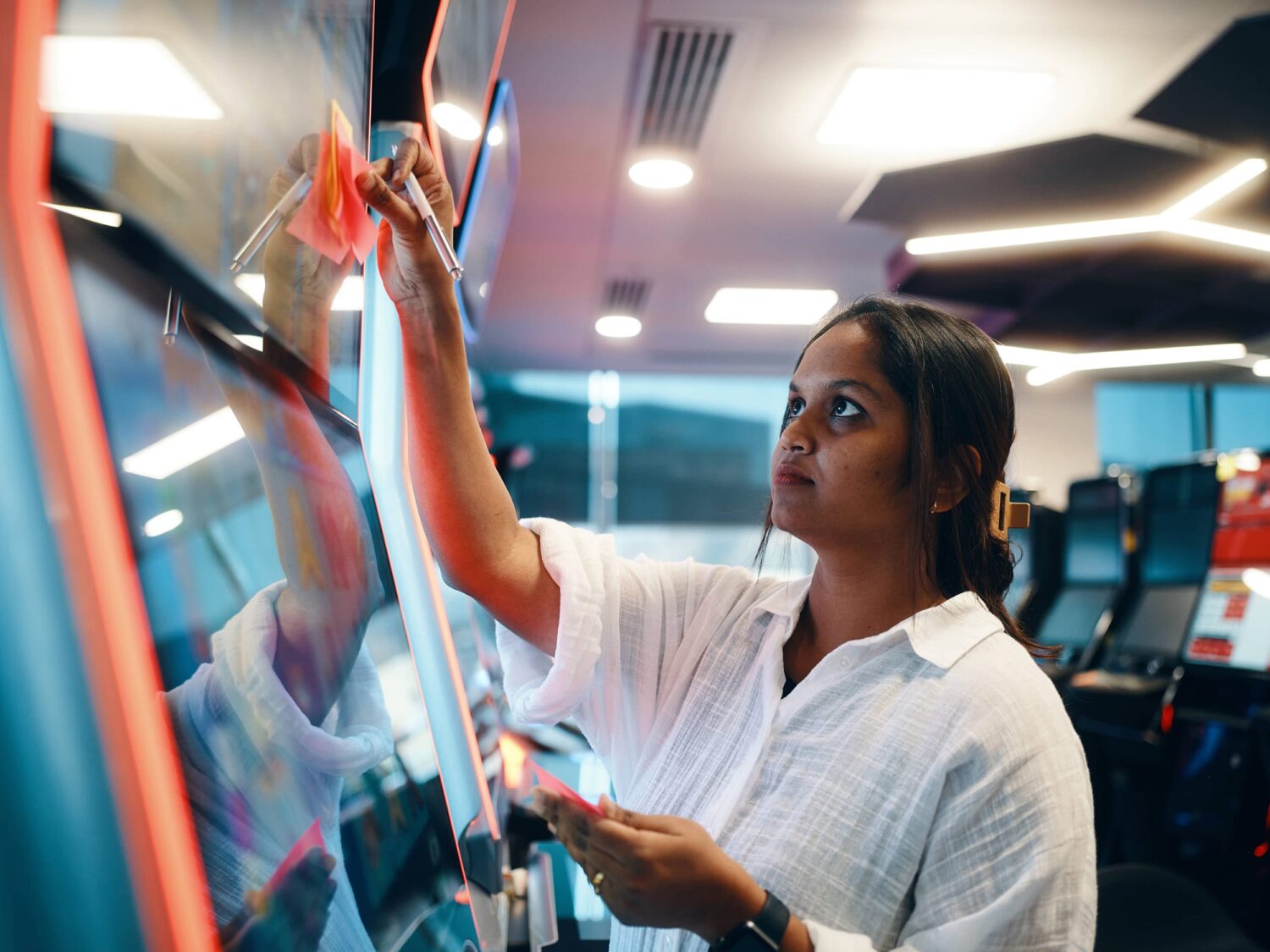 A woman in a white shirt cleaning a glass window inside a modern, well-lit interior.