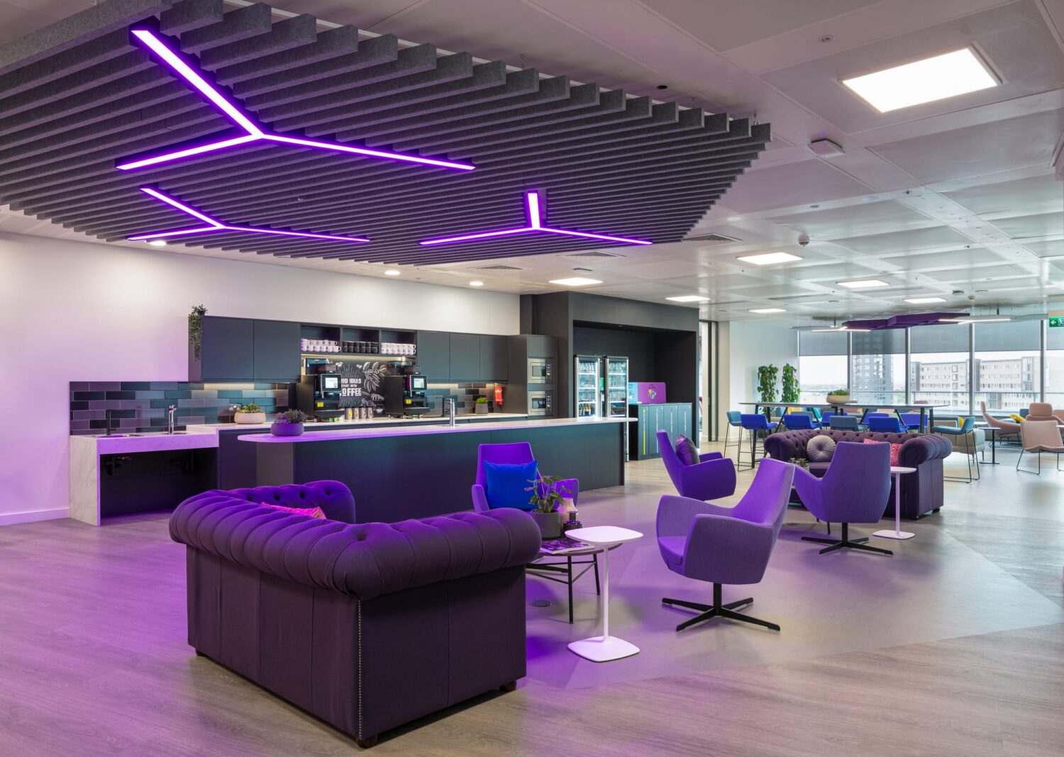 Modern open-plan lounge with purple seating, neon purple ceiling lights, and a service counter in the background.