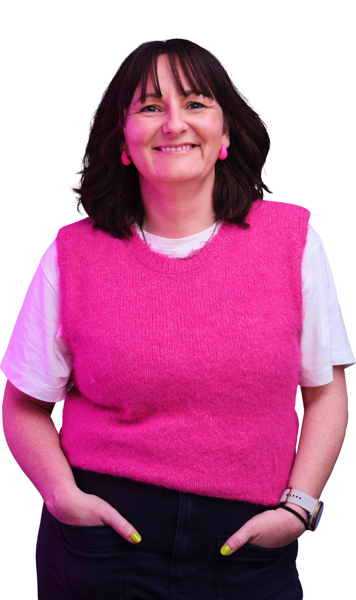 Smiling woman wearing a bright pink sleeveless sweater over a white shirt, with short dark hair and her hands in her pockets.
