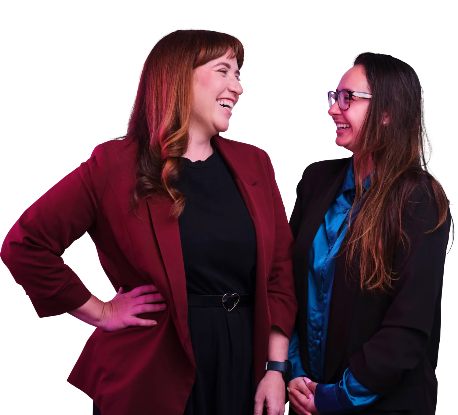 Two women are smiling at each other, one wearing a red blazer with black clothing and the other in a dark blazer with a blue blouse.