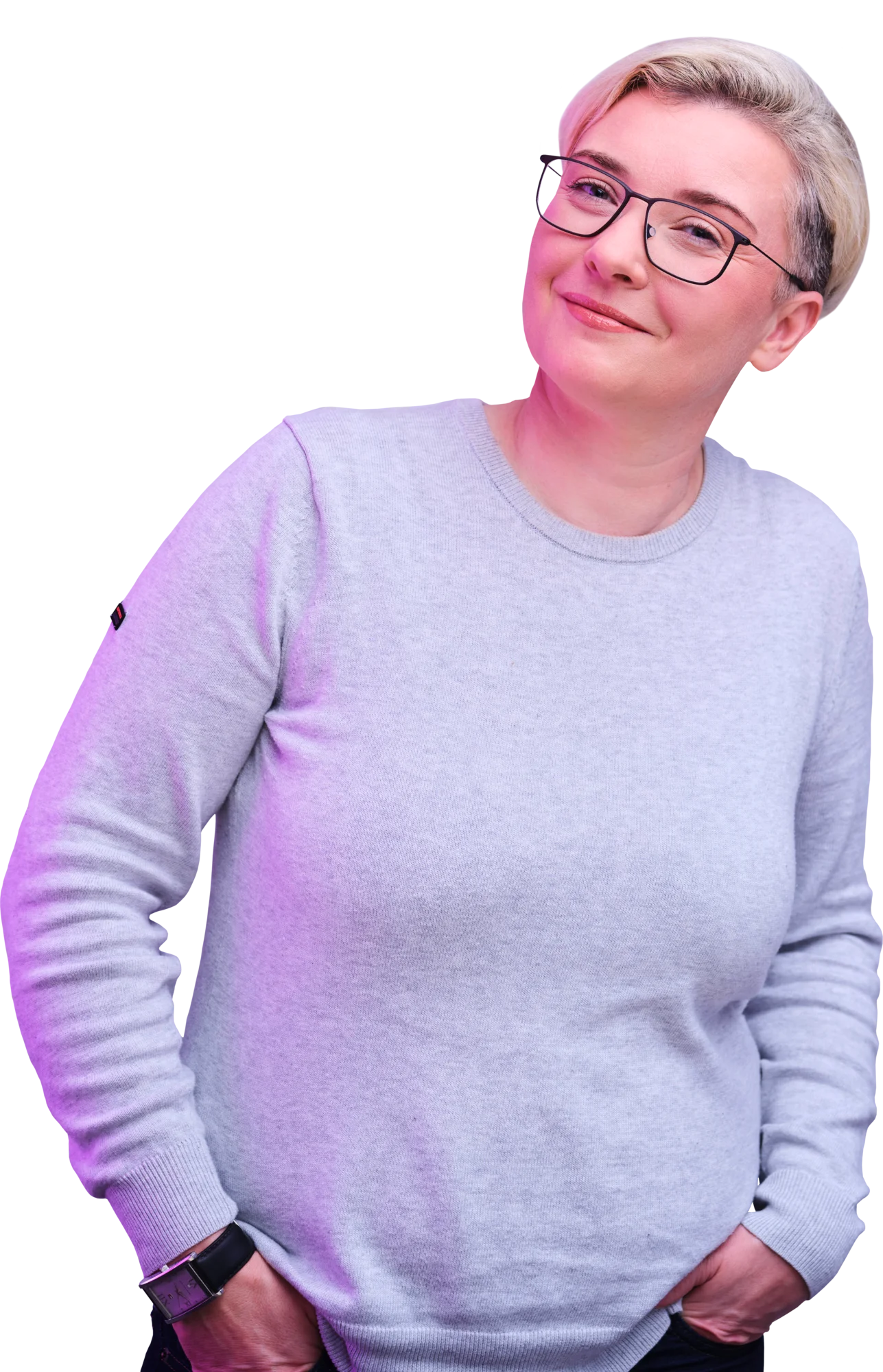 A woman with short gray hair and glasses wearing a light purple sweater, standing with her hands in her pockets.