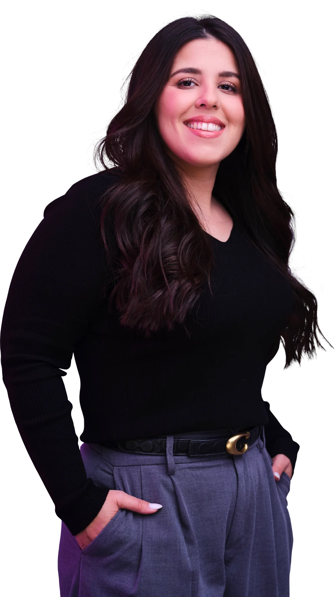 Smiling woman with long dark hair wearing a black top and blue pants, with her hands in her pockets.