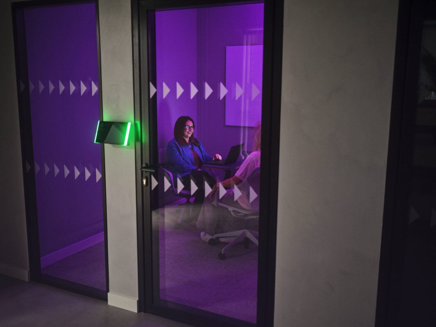 A person sits on a couch in a purple-lit room visible through glass doors, with a green exit sign nearby.