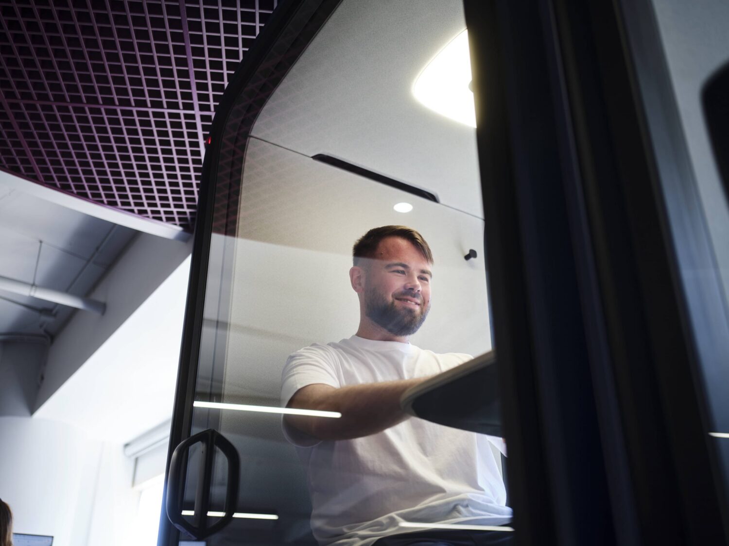 Smiling man sits in the driver's seat of a truck, steering inside the cab.