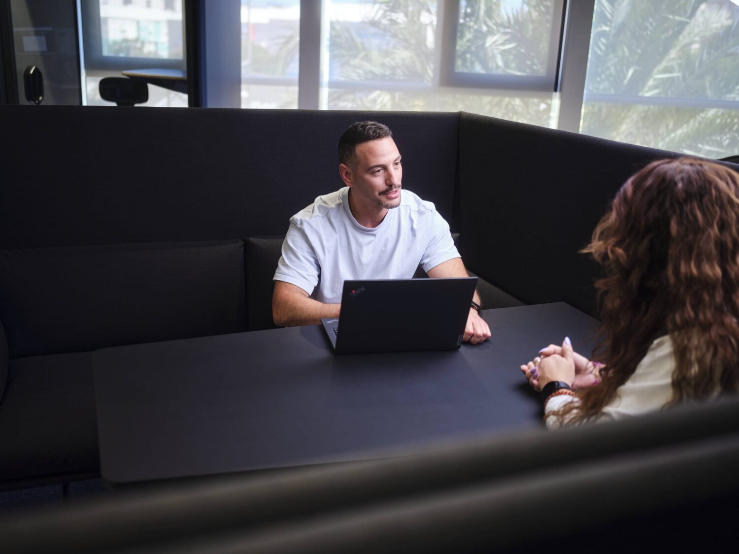 Man and woman sit across from each other at a booth-style table with a laptop.