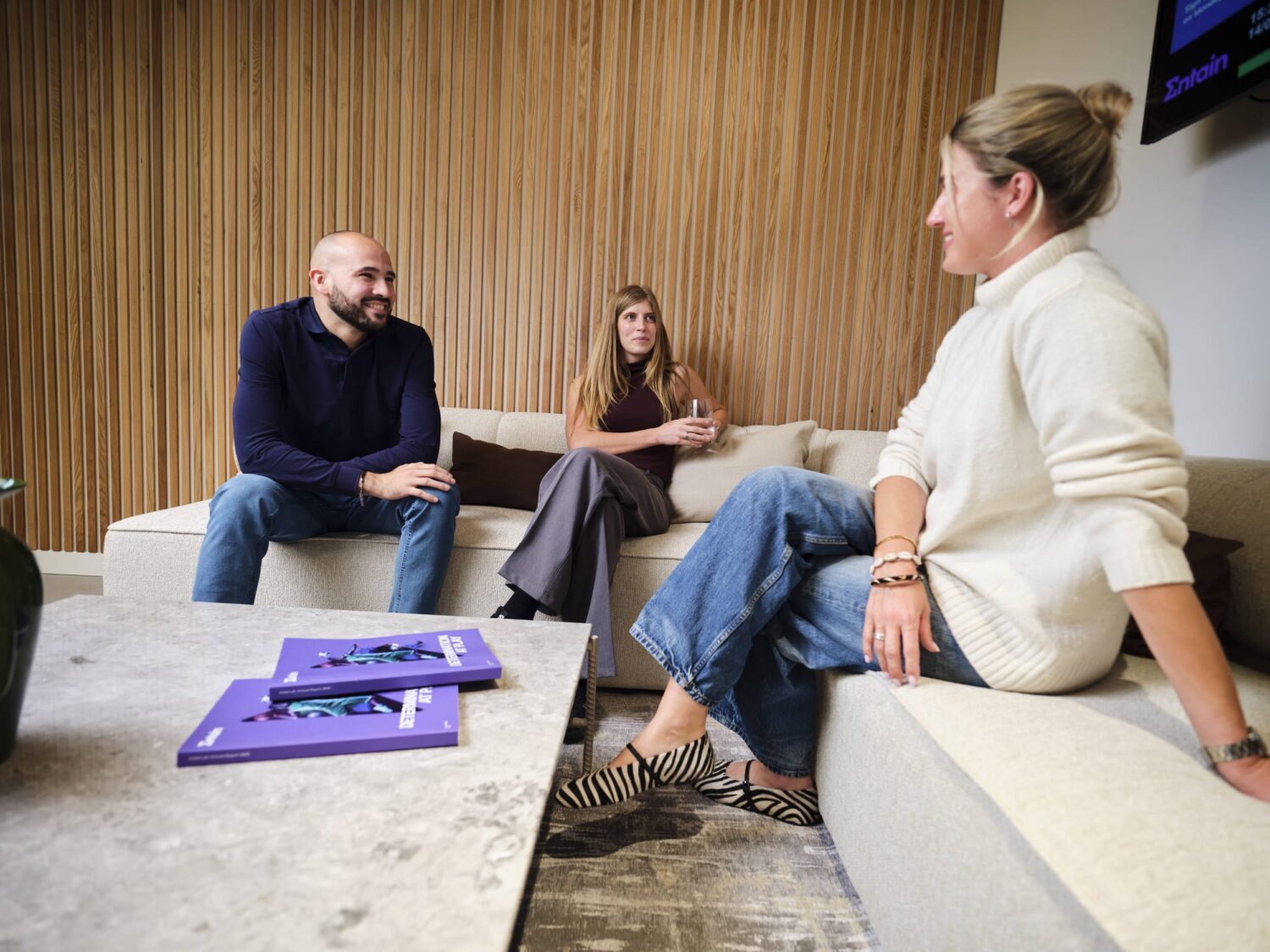 Three people sit and chat in a modern living room, with a purple binder on the coffee table.
