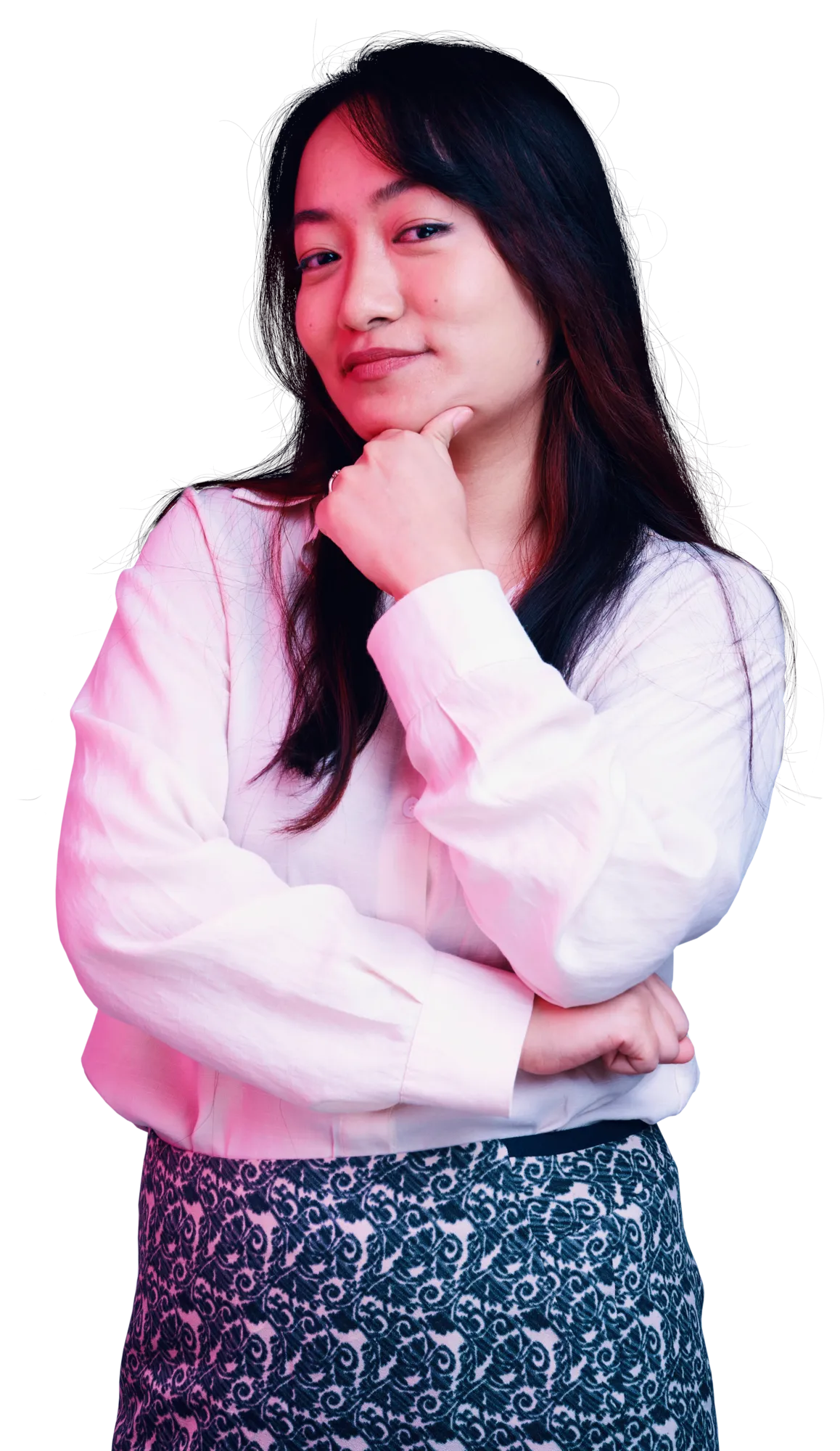 A woman with long dark hair wearing a light pink sweater and a patterned skirt poses with her chin resting on her hand.