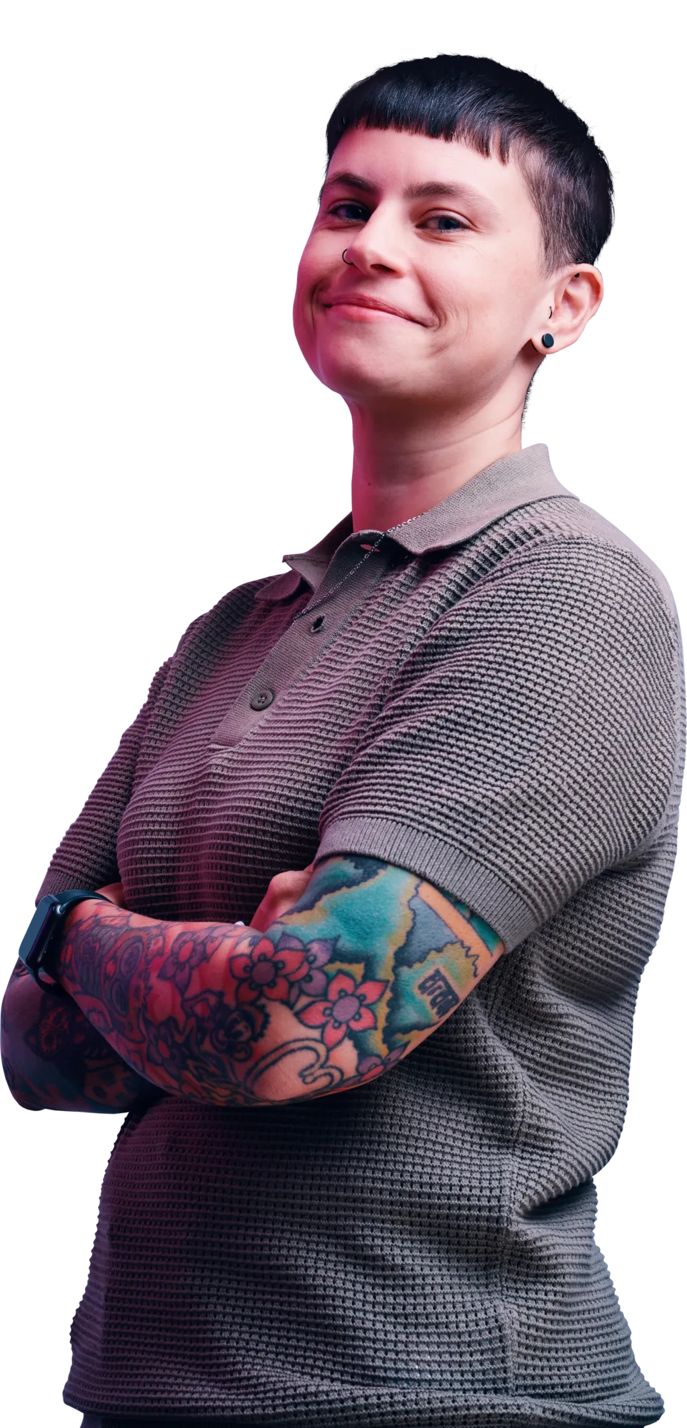 A person with short dark hair wearing a gray polo shirt, arms crossed, showing colorful tattoos on their forearms.