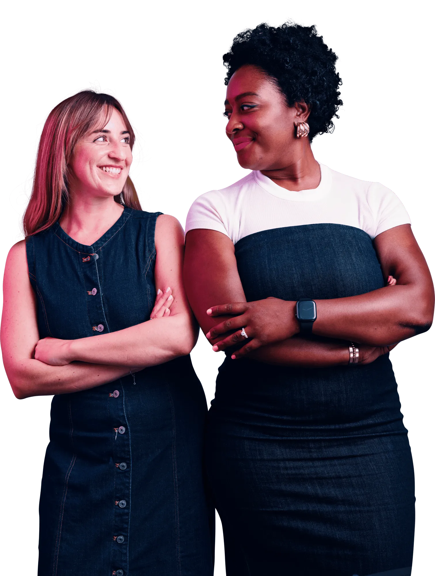 Two women standing side by side, smiling at each other with their arms crossed.
