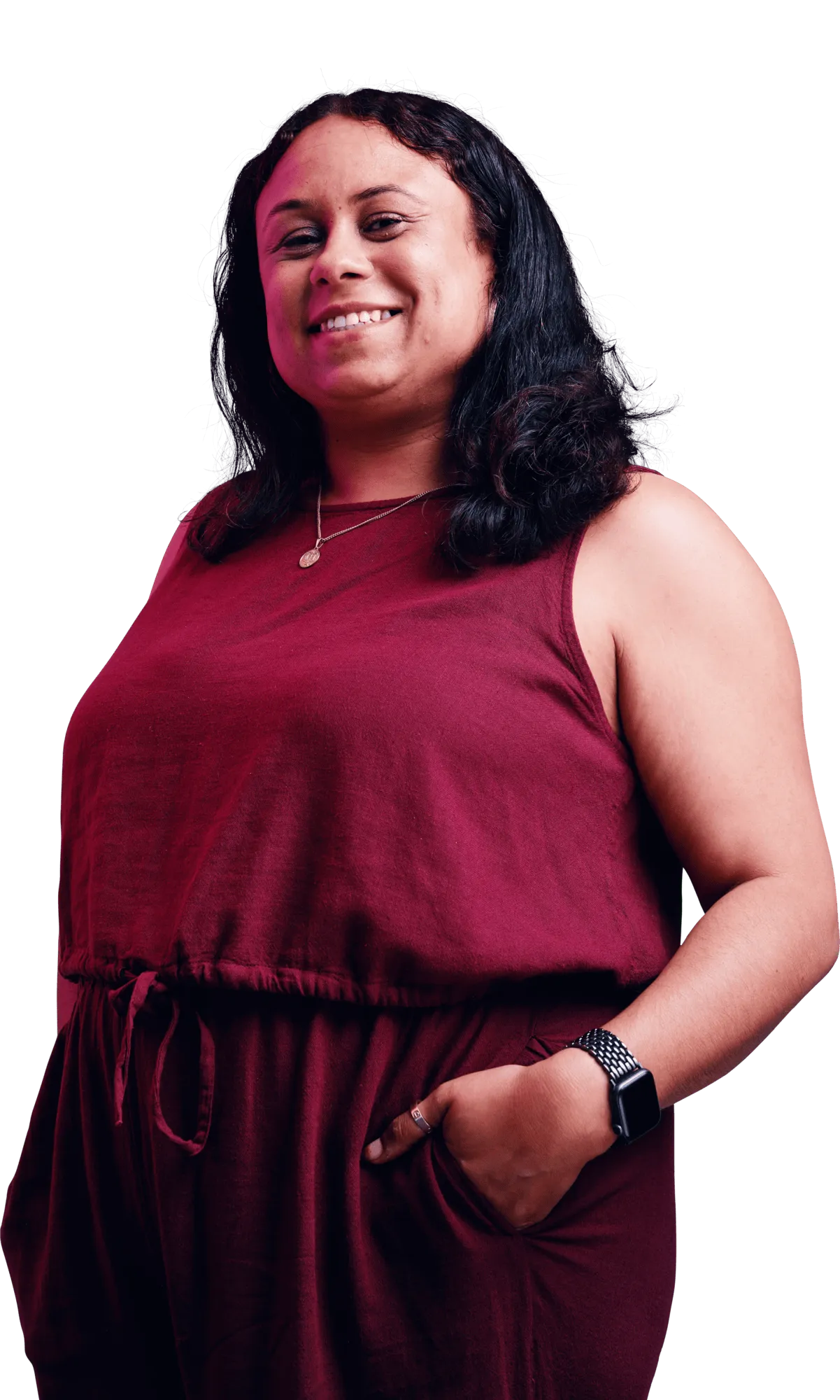 Smiling woman with dark, curly hair wearing a sleeveless maroon dress, with her hand in her pocket and a smartwatch on her wrist.