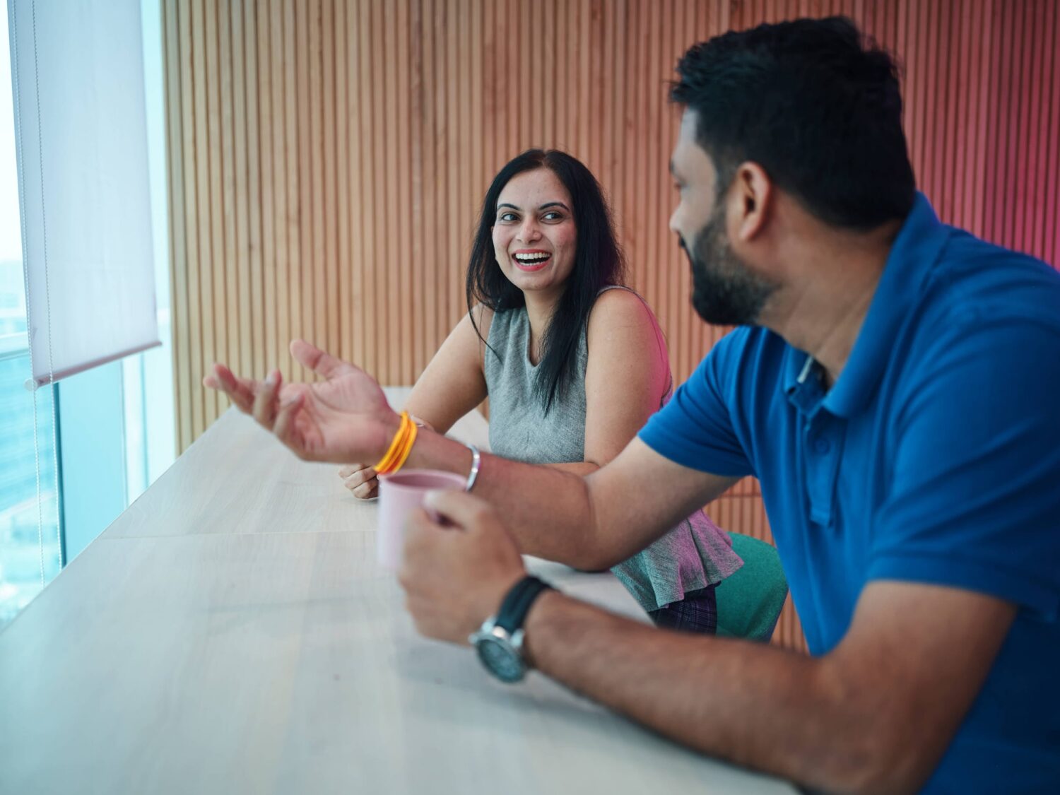 A woman and a man sit at a white table by a window, smiling and talking.