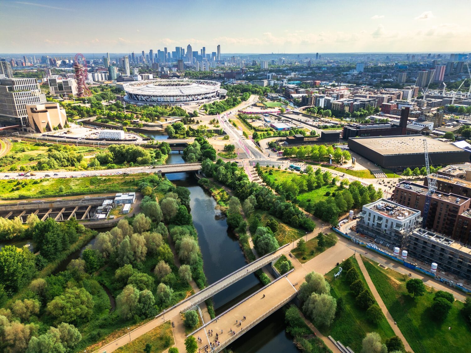 Aerial view of a city with lush green parks, a winding river with bridges, and a skyline of modern buildings in the distance.